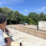 A person observes the Tomb of the Unknown Soldier at Arlington National Cemetery. A guard stands nearby, surrounded by greenery under a clear sky.