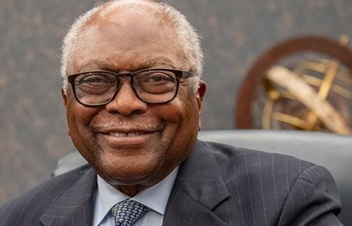 SC Rep. Jim Clyburn in a suit and glasses smiling, seated indoors with a decorative globe object in the background.